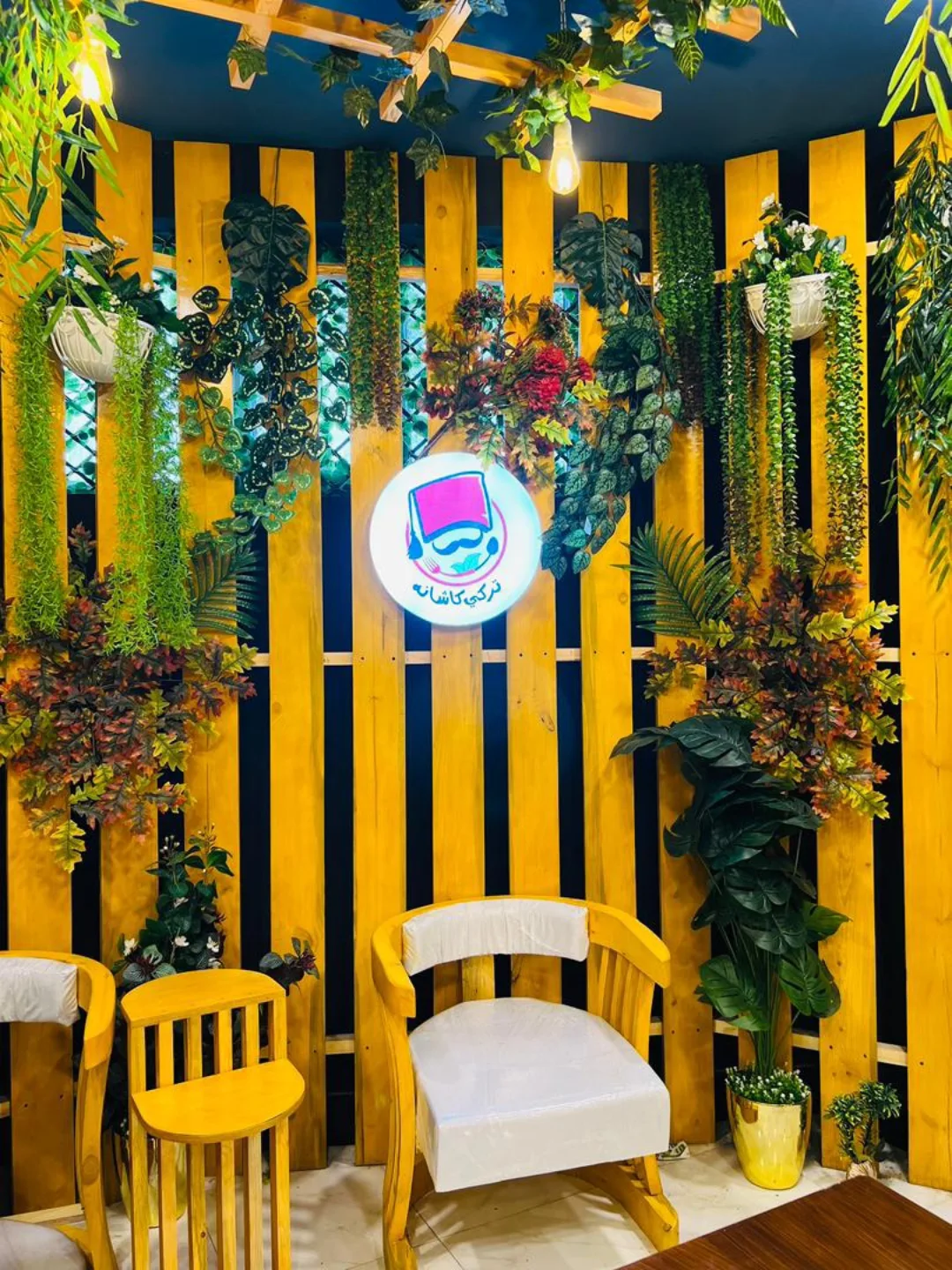 TURKEY KASHANA seating area with yellow wooden slats, hanging greenery and an illuminated sign